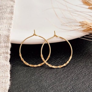 Könnte beinhalten: Ein Paar goldene Creolen mit einer strukturierten, gehämmerten Oberfläche. Die Ohrringe sind schlicht und elegant und wären ein tolles Geschenk.