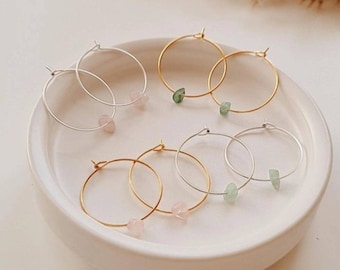 May include: Four pairs of hoop earrings with small gemstone accents. Two pairs are gold and two pairs are silver. The earrings are displayed on a white ceramic dish.