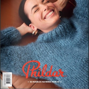 May include: A magazine cover featuring a woman wearing a blue fuzzy sweater. The magazine is titled "Phildar" and says "30 Modeles Matieres Nobles" on the bottom. The magazine cover also says "N° 204 A/H 2021-2022".