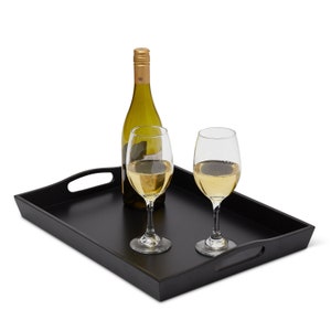 May include: A black rectangular serving tray with two wine glasses filled with white wine and a green wine bottle. The tray has two handles and is set against a white background. The wine bottle has a gold cap.