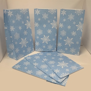 May include: A set of six blue paper gift bags with a white snowflake pattern. The bags are ideal for festive gift giving.