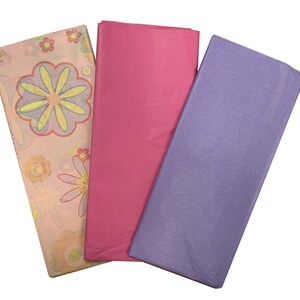 May include: Three sheets of tissue paper. One sheet is pink, one is purple, and one has a floral pattern with pink, yellow, and green flowers.