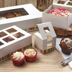 May include: A selection of white cardboard boxes with clear windows for displaying cupcakes and other baked goods. The boxes feature colourful striped designs and are ideal for packaging and presenting treats.