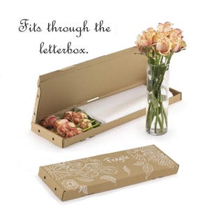 May include: A brown cardboard box with a floral design and the word "Fragile" in white. The box is closed and next to an open box containing pink roses and a white sheet. A glass vase with roses is also present. Text reads: Fits through the letterbox.