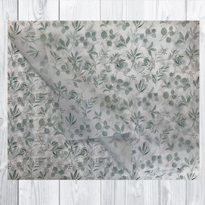 May include: White tissue paper with a repeating pattern of green leaves and branches. The paper is folded in half, showing the pattern on both sides.