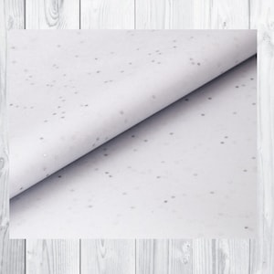 May include: White tissue paper with a subtle silver glitter pattern. The paper is folded in half, showing the pattern on both sides.