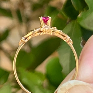 May include: A gold ring with a delicate design and a single red gemstone in the centre.