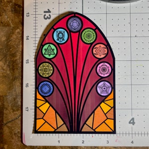 Puede incluir: Una pegatina de ventana de vitral con fondo rojo y un dise&ntilde;o colorido de formas geom&eacute;tricas y s&iacute;mbolos. La pegatina tiene forma de arco y un contorno negro.