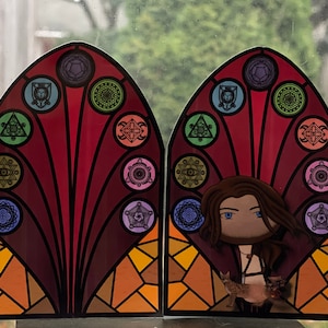 Puede incluir: Un dise&ntilde;o de vitral con un patr&oacute;n geom&eacute;trico colorido y un personaje con cabello largo y casta&ntilde;o y un gato. El dise&ntilde;o presenta un patr&oacute;n repetitivo de c&iacute;rculos y tri&aacute;ngulos con una figura central.