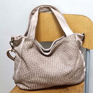 Könnte beinhalten: Eine hellbeige gewebte Ledertasche mit einem langen Riemen. Die Tasche liegt auf einem Holzstuhl.