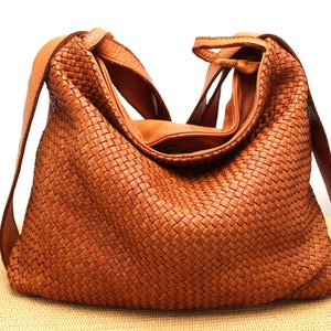 May include: A brown leather woven handbag with a long strap. The bag has a slouchy, casual look.