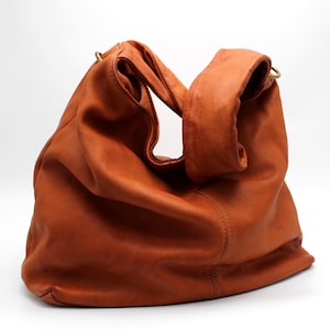 May include: A brown leather hobo bag with a slouchy design and two straps. The bag has a gold metal ring on each strap.