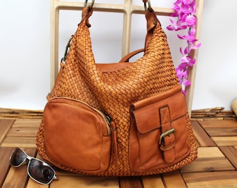 May include: A woven brown leather handbag with multiple pockets and a buckle closure. The bag is sitting on a wooden surface.