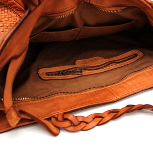 May include: A brown leather tote bag with a braided strap and a zippered pocket inside. The bag has a woven pattern on the front.