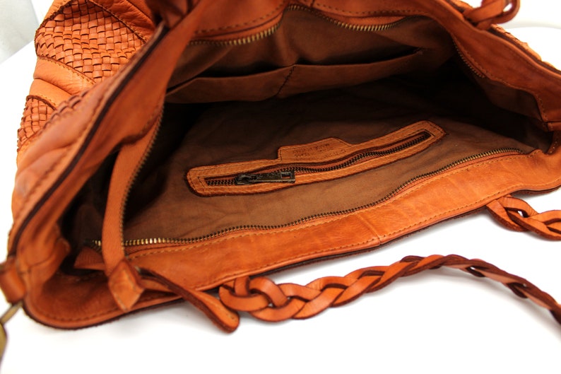 May include: A brown leather tote bag with a braided strap and a zippered pocket inside. The bag has a woven pattern on the front.