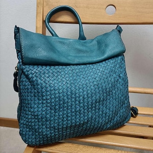 May include: A teal blue leather handbag with a woven design. The bag has a top flap and two handles.