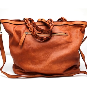 May include: A brown leather tote bag with a braided leather strap. The bag has a zippered pocket on the front and a long shoulder strap.
