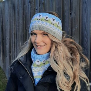 May include: A woman wearing a blue and white knitted headband with a sheep pattern and a matching blue and white knitted neck warmer. The headband and neck warmer are both made of a soft, cozy yarn.