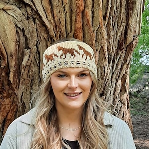 May include: A beige knit headband with a brown patterned design featuring stylized animals. The headband is worn by a person with long blonde hair.