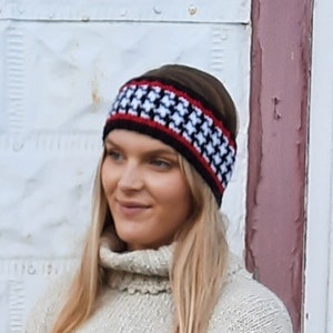 May include: A black and white houndstooth patterned headband with a red stripe. The headband is worn by a person with long blonde hair.