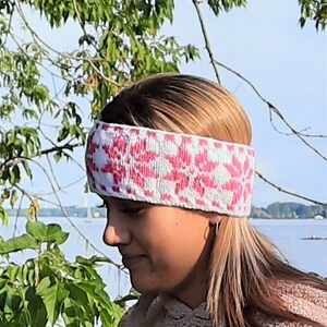 Può includere: Una donna indossa una fascia per capelli rosa e bianca con un motivo. La fascia è lavorata a maglia e ha un design geometrico.