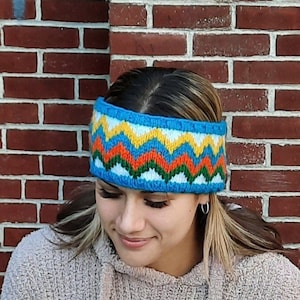 May include: A blue knitted headband with a colourful geometric pattern. The pattern features yellow, orange, green, and white zigzags.