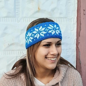 May include: A blue knitted headband with a white snowflake pattern. The headband is worn by a person with long brown hair.
