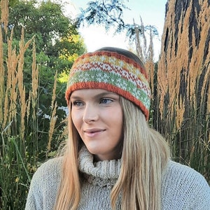 May include: A woman wearing a knitted headband with a colorful geometric pattern in shades of orange, green, white, and yellow. The headband is worn over her forehead and covers her ears. She is wearing a light gray turtleneck sweater.