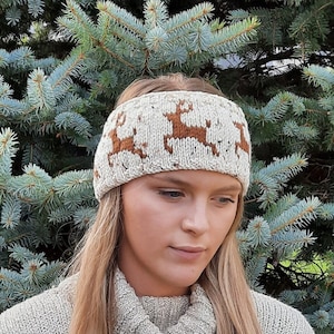 Puede incluir: Una diadema de punto blanco con un patrón de reno marrón. La diadema la lleva una persona con el pelo largo y rubio y un jersey blanco.