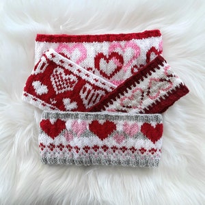 Op de afbeelding: Drie gebreide hoofdbanden met een Valentijnsdagthema. De hoofdbanden zijn rood, wit en roze met een hartjespatroon.