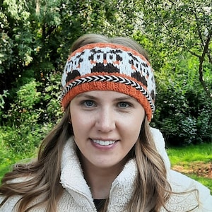 May include: A woman wearing a white fleece jacket with a brown zipper. She is wearing a knitted headband with a brown, white, and orange pattern.