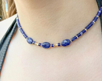 May include: A blue and gold beaded necklace with oval-shaped blue stones.