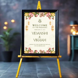 May include: A wedding welcome sign on a yellow easel. The black framed sign features floral arrangements and the text "WELCOME TO THE WEDDING" and the names "VIDANSHI & VIKRAM" with the date February 25, 2025.