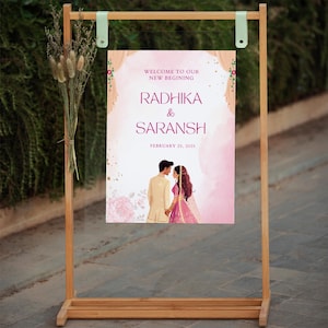 May include: A pink and white wedding welcome sign with a watercolour background. The sign features a couple in traditional Indian attire, with the text "Welcome to our new beginning Radhika & Saransh February 25, 2025".