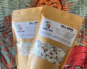 May include: Two brown paper bags with white labels. The labels have the text "LUV'S REMEDY SHOP" and "FULL MOON Herbal Bath Salt". The bags contain a white bath salt mixture with dried herbs and flowers.