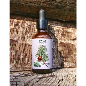 Può includere: Una bottiglia di vetro marrone con un contagocce e un'etichetta bianca. L'etichetta presenta un disegno di foglie verdi e il testo "Lucky Forest" e "Pine Needles Double Extraction Tincture".