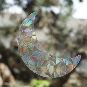 May include: A crescent moon-shaped window cling with a mosaic pattern in iridescent colors. The cling is made of a clear, translucent material and has a rainbow effect.