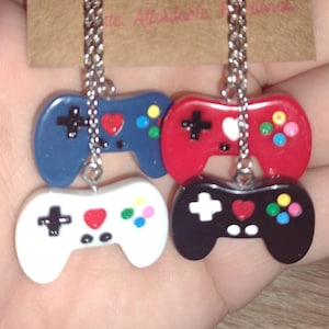 May include: Four colorful video game controller pendants on silver chains. The controllers are blue, red, white, and black, each with a heart and colorful buttons. The text in the background says "...te. Affordable. ...ional."