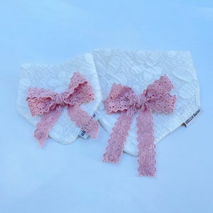 May include: Two white lace fabric dog bandanas with pink lace bows. The bandanas have the text "HELLO Butter" printed on them.