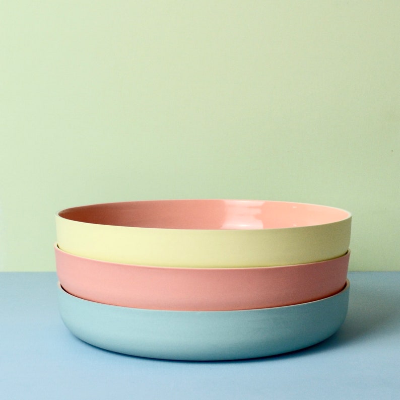 Może przedstawiać: Stos czterech ceramicznych misek w pastelowych kolorach. Miski są w odcieniach jasnoniebieskiego, r&oacute;żowego i ż&oacute;łtego. Miski są ułożone jedna na drugiej, z niebieską miską na dole i ż&oacute;łtą miską pośrodku.