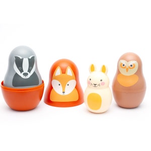 Op de afbeelding: Een set van vier houten nesting dolls met bosdierontwerpen. De poppen bevatten een das, een vos, een konijn en een uil, elk met een uniek kleurenschema en gezichtsuitdrukking. De das is grijs en wit, de vos is oranje, het konijn is crème en de uil is bruin.