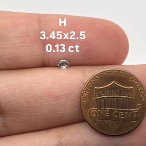 May include: A small, oval-shaped gemstone with a light green hue, next to a United States one-cent coin. The gemstone is labeled with the measurements 3.45x2.5 and 0.13 ct. The letter "H" is above the measurements.