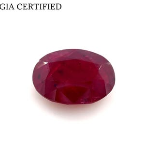 May include: A deep red, oval-cut ruby gemstone, with multiple facets. The gem is set against a white background. The text "GIA CERTIFIED" is at the top of the image.