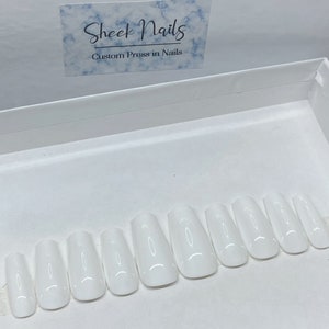 Pu&ograve; includere: Un set di dieci unghie finte bianche lucide disposte in fila all'interno di una scatola bianca. Sopra le unghie, un cartoncino rettangolare presenta un motivo a marmo blu con il testo Sheek Nails Custom Press in Nails stampato in inchiostro nero.