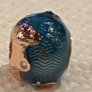 May include: A blue and rose gold charm with a wave pattern and a rose gold flower design.