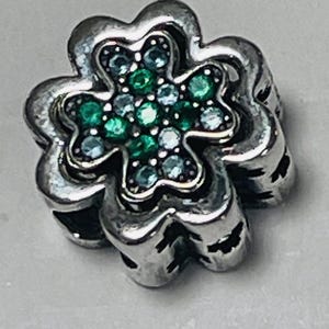 May include: Silver charm in the shape of a four-leaf clover with green and blue crystals.