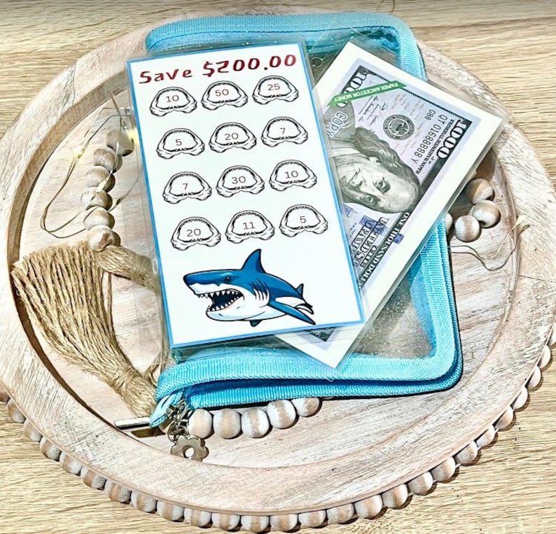 May include: A blue zippered pouch with a clear plastic window containing a shark tooth chart and a $1000 bill. The chart has a shark graphic and the text "Save $200.00".