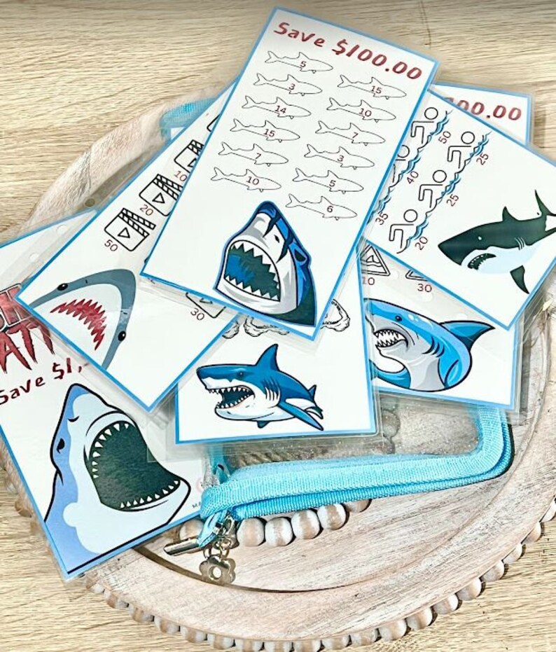 May include: A set of colorful shark-themed educational flash cards with different amounts of money on each card. The cards are in a clear plastic pouch with a blue zipper.