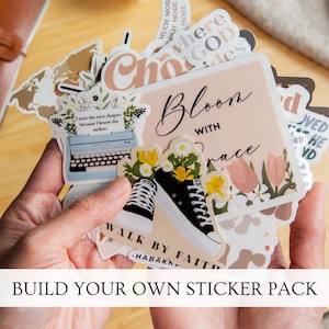 May include: A collection of assorted vinyl stickers featuring various designs including a typewriter with flowers, black trainers with daisies, and text-based graphics such as Bloom with Grace and Walk by Faith, all displayed in a layered stack.