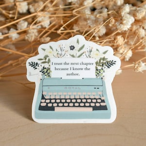 May include: A blue typewriter sticker with a floral design and the quote "I trust the next chapter because I know the author."